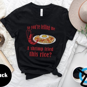 May include: Black t-shirt with a red shrimp and fried rice illustration. The text on the shirt reads "so you're telling me a shrimp fried this rice?"
