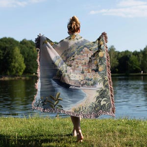a woman is holding a blanket in front of a body of water
