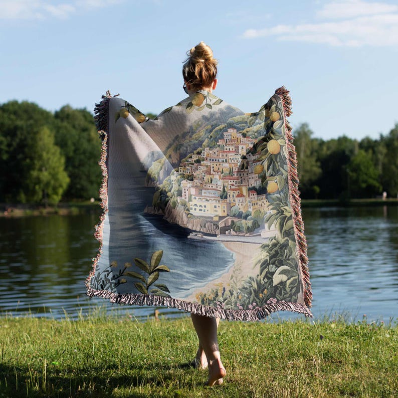 a woman is holding a blanket in front of a body of water