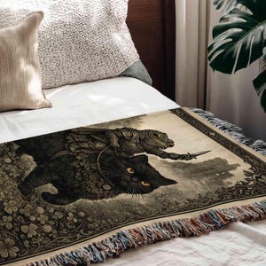 a black cat with yellow eyes and a frog riding on its back, both depicted on a blanket with a detailed, artistic illustration.