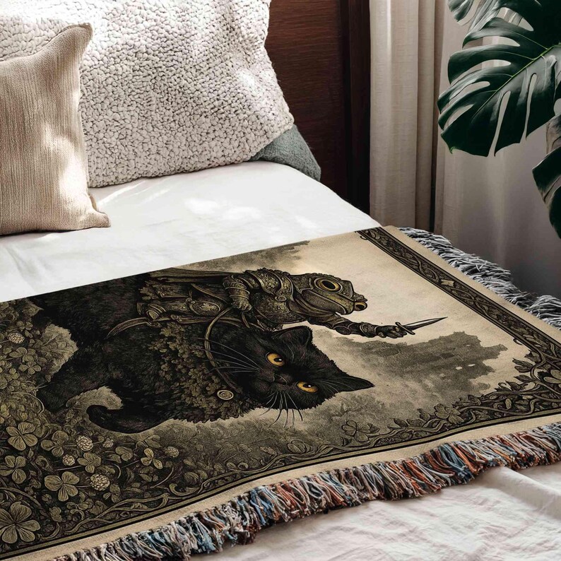 a black cat with yellow eyes and a frog riding on its back, both depicted on a blanket with a detailed, artistic illustration.