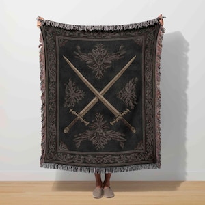 A person is standing in front of a white wall, holding a large, ornate blanket with a design of crossed swords.