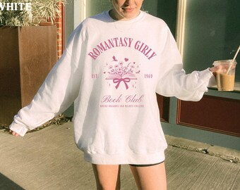 May include: White long-sleeved sweatshirt with a pink graphic design that says "Romantasy Girly Est. 1969 Book Club Where Dreams and Hearts Collide".