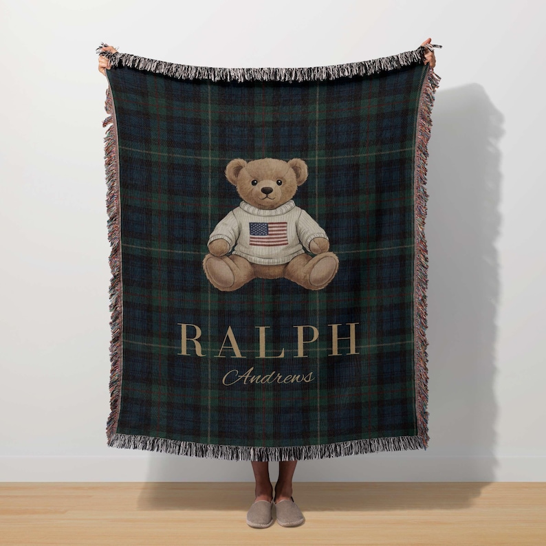 A person is standing in front of a large blanket with a teddy bear wearing a sweater and an American flag design.