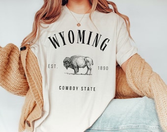 May include: A white t-shirt with a black graphic design that says "WYOMING EST. 1890 COWBOY STATE" with a drawing of a buffalo in the center.