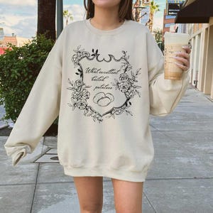 May include: A cream-colored sweatshirt with a black graphic print of a floral design and the text "What excellent boiled potatoes".