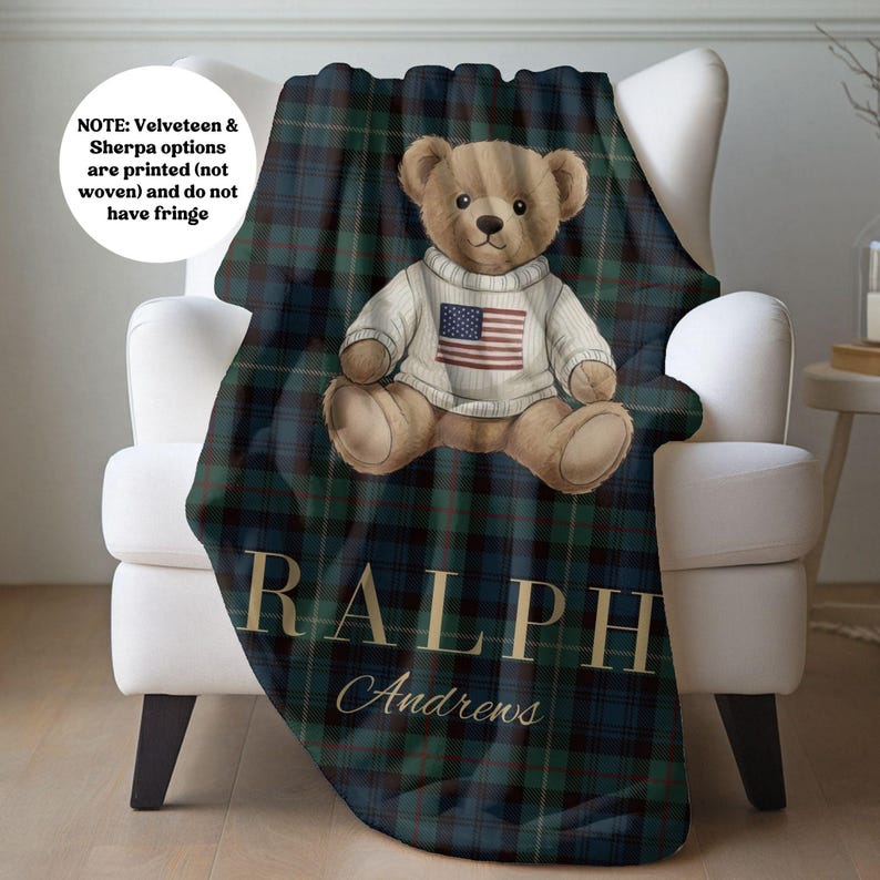 May include: A dark green and navy blue plaid blanket featuring a central illustration of a brown teddy bear wearing a white sweater with an American flag graphic. The text RALPH Andrews is printed in gold lettering below the bear. NOTE: Velveteen & Sherpa options are printed (not woven) and do not have fringe.