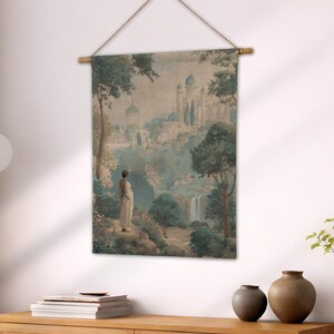 May include: A wall hanging featuring a serene landscape with a woman in a white gown. The artwork depicts a castle, trees, and a waterfall in shades of blue, green, and beige. The tapestry is suspended from a wooden rod with a natural fiber cord.