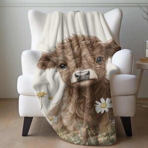 A cozy blanket featuring a close-up of a cow's face with a floral pattern, including white flowers and green foliage.