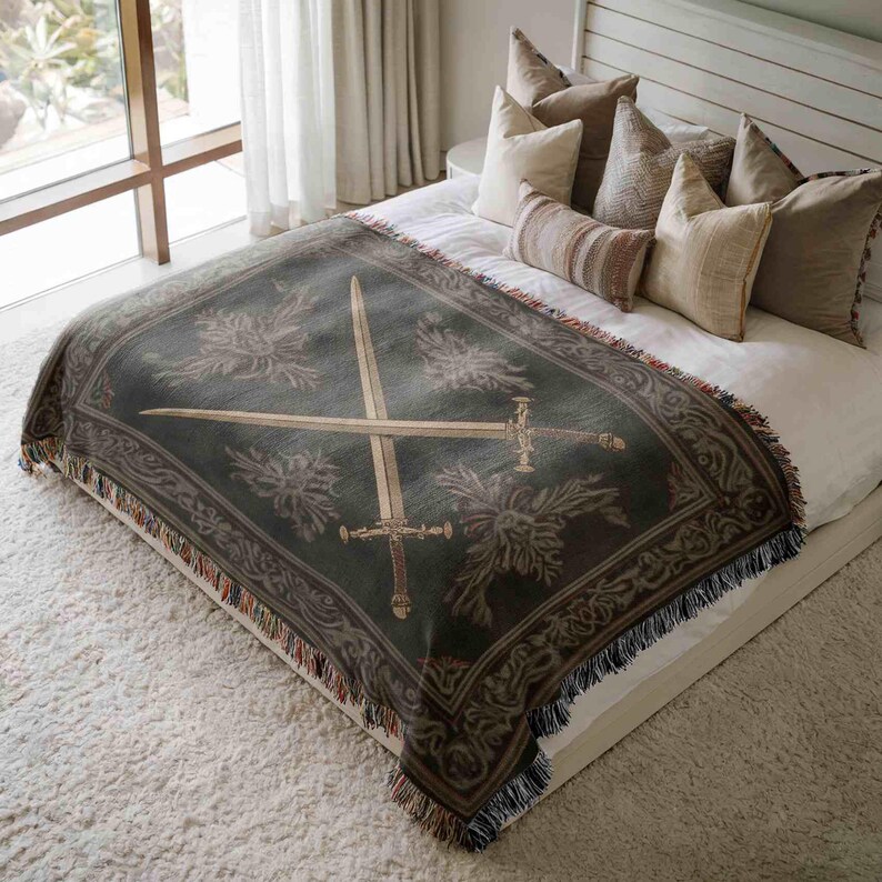 a bedroom with a large bed covered in a decorative blanket featuring a sword design. The bed is surrounded by pillows, creating a cozy and inviting atmosphere.