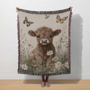 A person is standing in front of a large blanket that features a cow surrounded by flowers and butterflies.