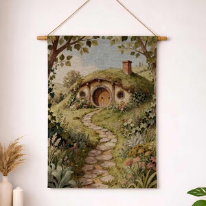 May include: A tapestry wall hanging depicting a hobbit hole nestled in a lush, green hillside. A stone path leads to the round wooden door. The scene is framed by trees and foliage, with a blue sky peeking through.
