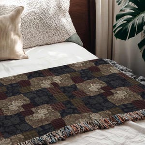 May include: A patchwork throw blanket with a floral and plaid pattern in shades of brown, navy, and burgundy. The blanket has a fringed edge and is displayed on a bed with pillows.