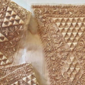 May include: Close-up of beige lace fabric with intricate floral and geometric embroidery. The lace features a delicate, open weave with detailed patterns and a soft, neutral colour, suitable for various craft projects.