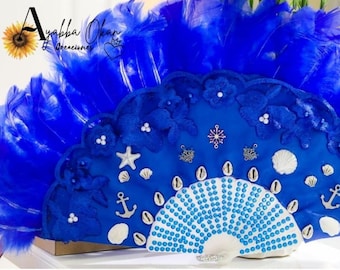 Peut inclure: Un éventail bleu et blanc sur le thème des coquillages et des ancres. L'éventail est décoré de plumes bleues, de coquillages blancs et de perles bleues et blanches. L'éventail est en tissu et a un manche en bois.