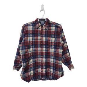 Peut inclure: Chemise à carreaux à manches longues, boutonnée, dans un motif à carreaux classique. La chemise présente une palette de couleurs bordeaux, bleu marine, crème et sarcelle. Suspendue à un cintre blanc.