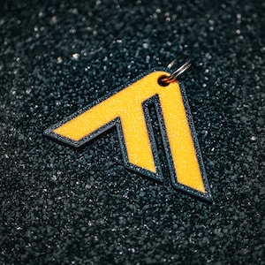 May include: A yellow arrow-shaped keychain with a black outline and a silver ring. The keychain is made of a textured material and has a shiny finish.