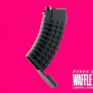 Może przedstawiać: Szary plastikowy zapalniczkowy pojemnik do przechowywania w kształcie magazynka z nadrukiem "FUZED LABS WAFFLEMAG LIGHTER + STASH CASE" na spodzie.