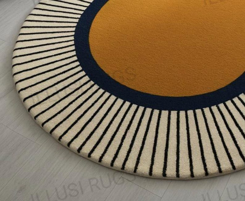 May include: A round rug with a mustard yellow center, a navy blue border, and a cream-colored outer ring with black vertical stripes. The rug has a soft, textured appearance and a modern design.