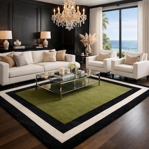 May include: A modern living room featuring a green rug with black and white borders. The room includes a white sofa, armchairs, and a glass coffee table. A chandelier hangs above, and a large window offers an ocean view.