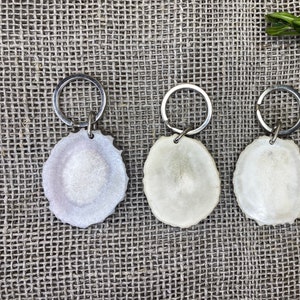 May include: Three white antler keychains with silver key rings. The keychains are oval shaped and have a smooth, polished finish.