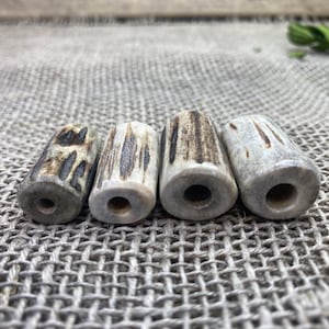 May include: Four natural bone beads with a light brown and dark brown striped pattern. The beads are cylindrical and have a hole drilled through the center.