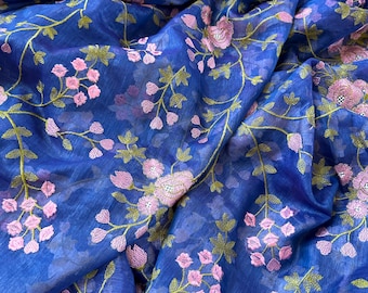 Pode incluir: Um tecido azul transparente com bordado floral rosa. O tecido tem um padrão listrado sutil e uma borda dourada.