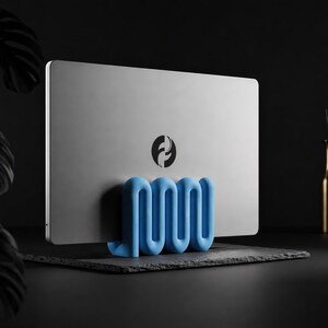 Könnte beinhalten: Ein silberner Laptop mit einem kreisförmigen schwarz-weißen Logo in der Mitte wird von einem hellblauen, wellenförmigen, serpentinenartigen Ständer aufrecht gehalten. Der Ständer hat ein durchgehendes, sich wiederholendes S-Kurven-Design.