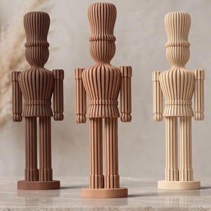 Peut inclure: Trois figurines de casse-noisettes debout alignées, chacune présentant un design à côtes verticales. Les personnages sont de couleur marron foncé, marron moyen et beige clair, et chacun repose sur une base circulaire avec un grand chapeau.