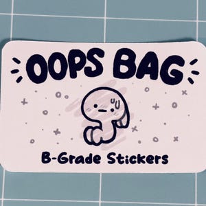 May include: A rectangular white sticker with rounded corners featuring the black text OOPS BAG at the top and B-Grade Stickers at the bottom. In the center is a small, simple black and white illustration of a worried character with a sweat drop.