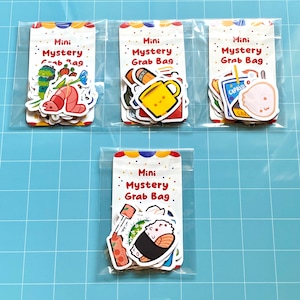 May include: Four clear plastic bags each containing a set of colorful stickers with the text "Mini Mystery Grab Bag". The stickers feature various designs including a caterpillar, a shrimp, a cup of coffee, a sushi roll, and a cartoon character.
