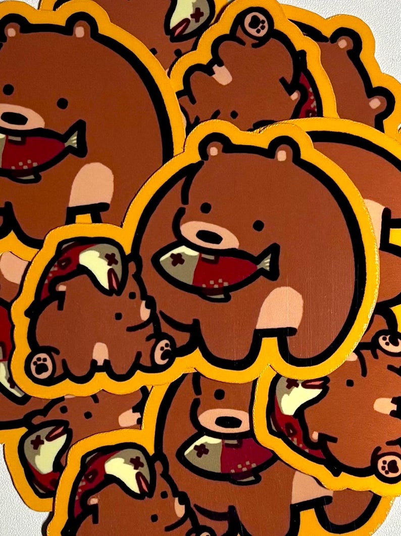 K&ouml;nnte beinhalten: Eine Ansammlung von braunen B&auml;ren-Aufklebern mit gelben Umrandungen. Jeder B&auml;r h&auml;lt einen rot-wei&szlig;en Fisch. Die Aufkleber sind im Cartoon-Stil gehalten.
