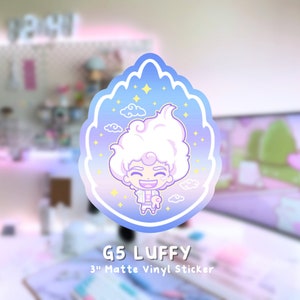 May include: A 3-inch matte vinyl sticker featuring a cartoon character with white hair, a blue shirt, and a pink animal in their hand. The character is surrounded by clouds and stars on a blue and purple gradient background. The text "G5 LUFFY" and "3" Matte Vinyl Sticker" is below the sticker.