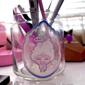May include: A glass jar with a holographic sticker of a cartoon character with white hair, a pink shirt, and a blue background. The sticker has a cloud and star design.