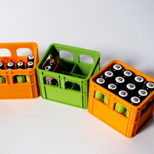 Könnte beinhalten: Drei Plastikkisten, eine grün und zwei orange, gefüllt mit AA-Batterien. Die Kisten haben ein Gittermuster und sind so konzipiert, dass die Batterien aufrecht stehen.