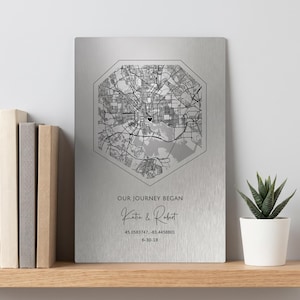 May include: A rectangular brushed silver metal plaque featuring a black octagonal street map print. The text reads OUR JOURNEY BEGAN, Katie & Robert, 45.0583747, -83.4458801, and 6-30-18. A small black heart icon marks a location on the map.