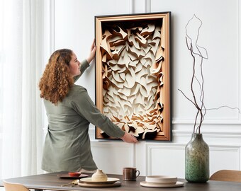 May include: A person hangs a framed abstract art print on a white wall. The print features a layered, textured design in shades of brown and white.