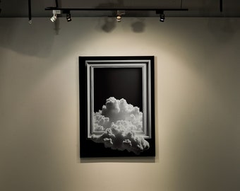 May include: A black and white photograph of a cloud formation framed in a black and white frame. The photograph is hanging on a white wall.