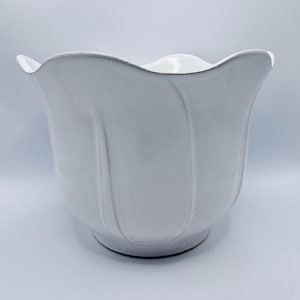 May include: A white ceramic planter with a scalloped rim and vertical ribbed detailing. The planter has a rounded base and a tulip-like shape. The interior is also white, and the overall design is simple and elegant.