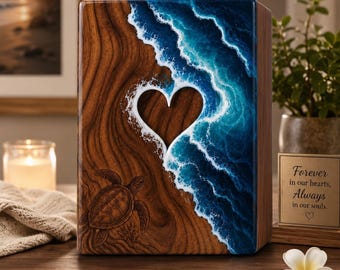 May include: A rectangular wooden cremation urn featuring a resin ocean scene with white waves crashing against a sandy shore. A heart-shaped cutout sits in the center, and a sea turtle is etched into the wood. A small sign reads: Forever in our hearts, Always in our souls.
