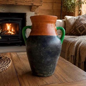 Könnte beinhalten: Eine zweifarbige Keramikvase mit einem breiten, bauchigen Körper, einer dunkel gesprenkelten anthrazitfarbenen Basis und einem glatten, warmen terrakotta-orangen Oberteil. Das Gefäß verfügt über zwei symmetrische grüne Henkel an den Seiten.