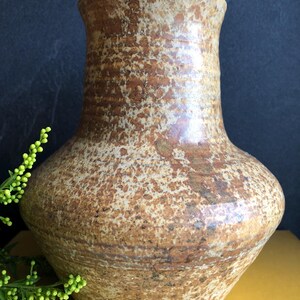 May include: A brown ceramic vase with a speckled pattern. The vase has a wide base and a flared rim. The surface has a textured appearance with shades of light and dark brown. A decorative item.