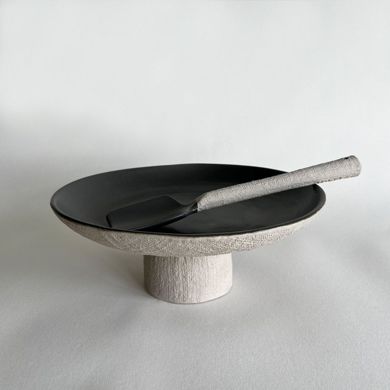 May include: A black ceramic cake stand with a white pedestal base and a matching black serving spatula.