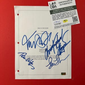 May include: A white Back to the Future film script page with three-hole punches on the left side, featuring blue ink signatures and a London Autograph Registry certificate of authenticity with a QR code and a holographic sticker attached.
