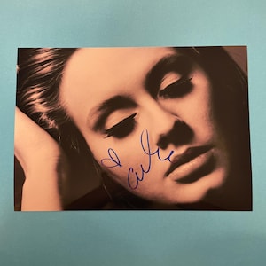 Puede incluir: Fotografía en primer plano de un rostro con los ojos cerrados y un fondo suave. La imagen está firmada con un bolígrafo azul, incluyendo un símbolo de corazón y el nombre "Adele".