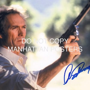Pode incluir: Fotografia de um homem segurando uma arma, com uma assinatura em tinta azul. A imagem tem o texto "DO NOT COPY MANHATTAN POSTERS" em branco. O homem está vestindo uma camisa branca com gola.