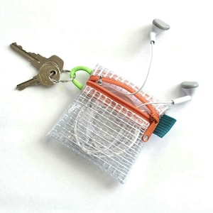 May include: A small, square, translucent white mesh pouch with an orange zipper closure. A lime green loop is attached to the side, holding two silver metal keys. White wired earbuds are stored inside the pouch with the cord extending outward.