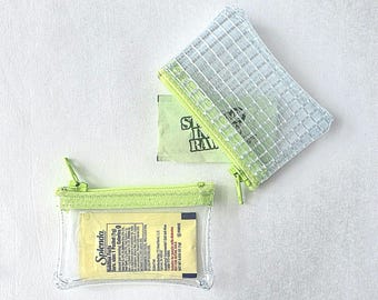 May include: Two small rectangular zip pouches with lime green trim. One pouch is made of clear plastic containing a yellow Splenda packet. The other pouch is made of a translucent white grid-patterned material containing a green Sugar In The Raw packet.