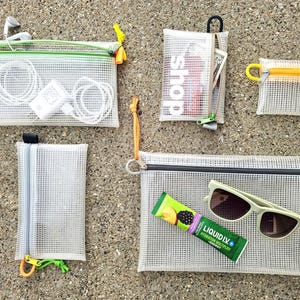 May include: A collection of clear mesh zippered pouches in various sizes. Some pouches contain items like headphones, a charger, money, and sunglasses. The pouches have colorful zippers and accents, including green, yellow, and orange.