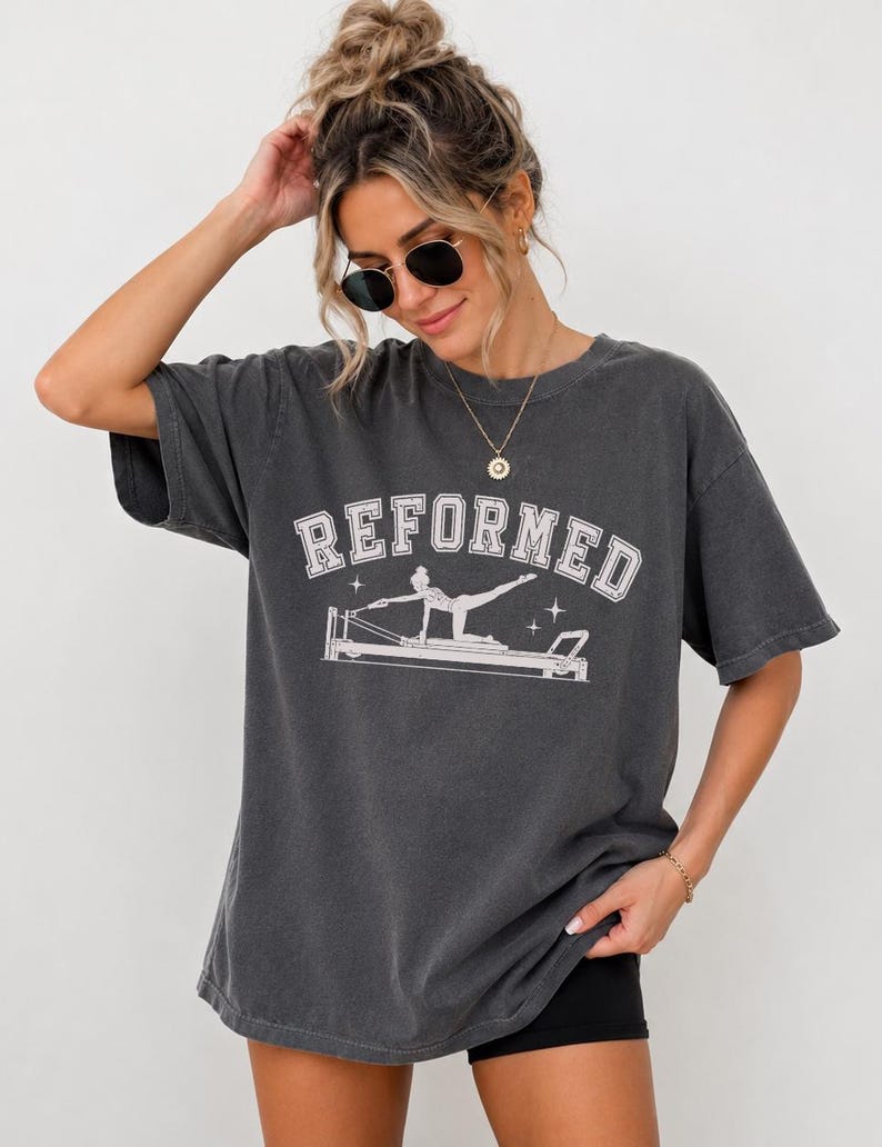 A woman wearing a gray t-shirt with the word "REFORMED" printed on it, posing with her hand on her head.